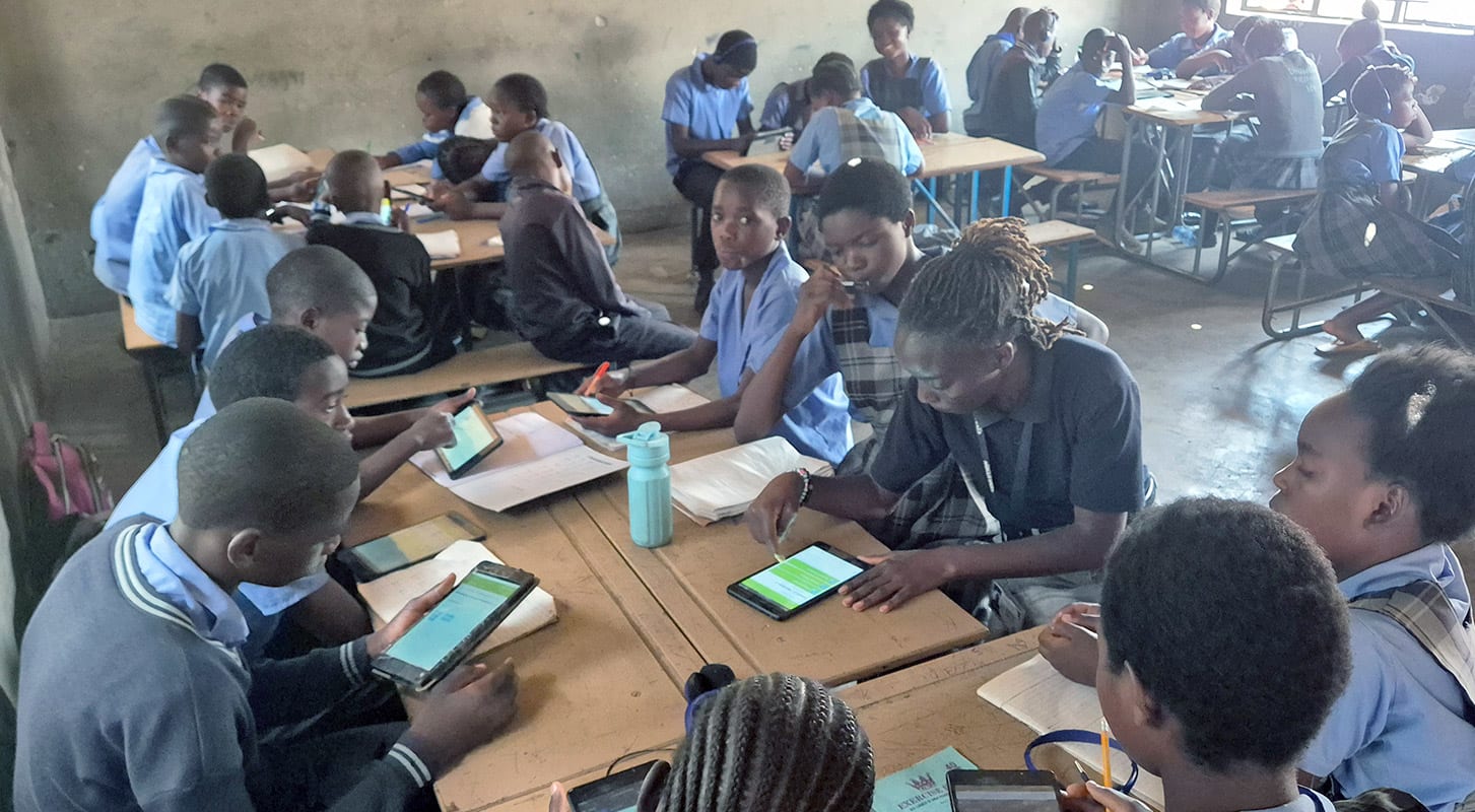 A group of children focused on their tablets while sitting at desks in a classroom setting.
